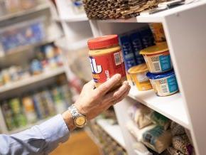 A hand places a jar of peanut butter on a shelf in the LR food pantry.